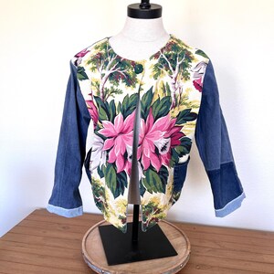 May include: A denim jacket with floral fabric panels on the front and back. The jacket has a button closure and long sleeves.