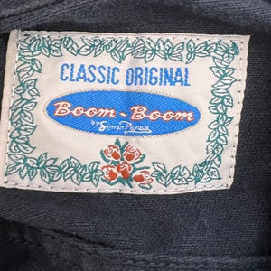 May include: A white label with green leaves and red roses around the border. The label says "Classic Original Boom-Boom by Simon Pava" in blue and black text.