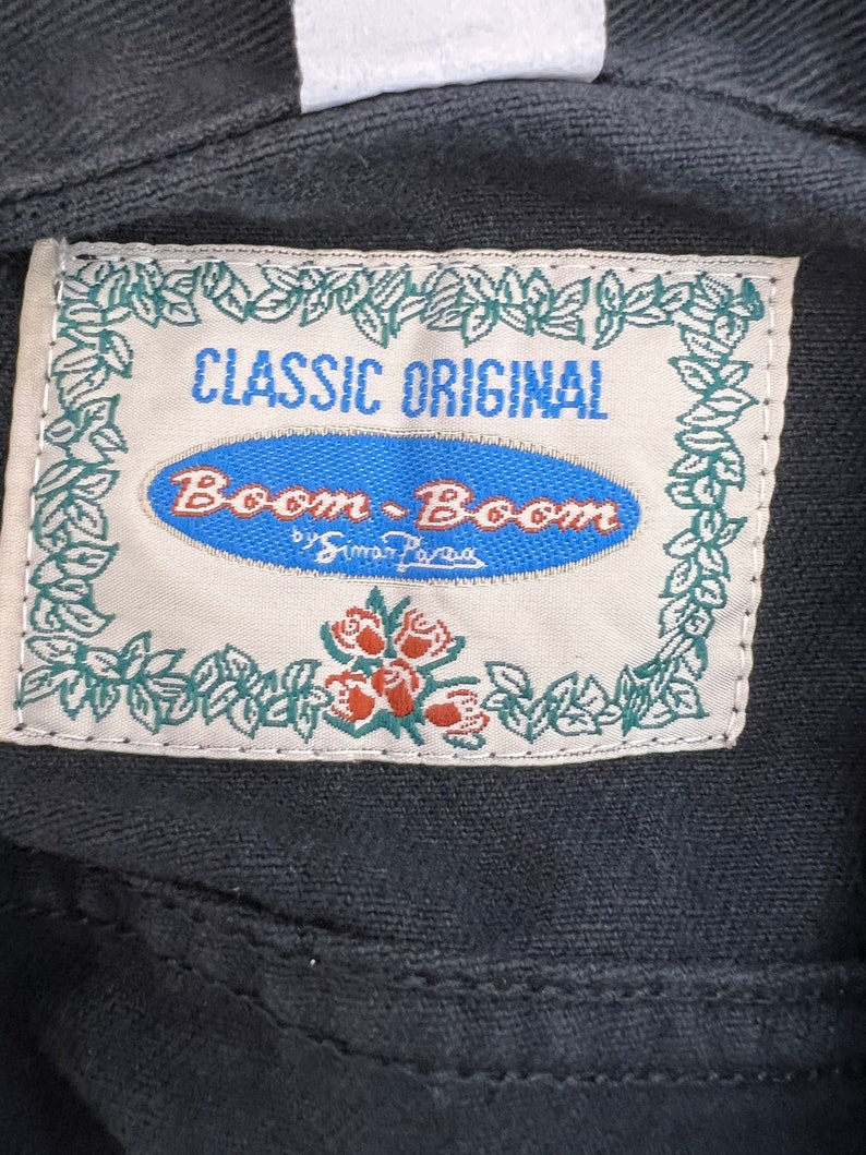 May include: A white label with green leaves and red roses around the border. The label says "Classic Original Boom-Boom by Simon Pava" in blue and black text.