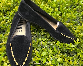 May include: A pair of black suede flats with gold stitching. The shoes have a pointed toe and a simple design.