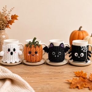 May include: Four white ceramic mugs, each featuring a unique, hand-crocheted cosy. The designs include a white ghost, an orange pumpkin with a green stem, a black bat with purple-lined ears, and a black spider with a white web and dangling charm.