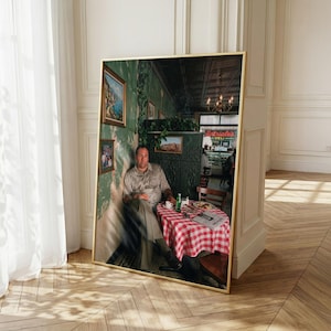 May include: A large framed print featuring a man sitting at a table with a red and white checkered tablecloth. The scene depicts an interior with green walls, framed pictures, and a view of a storefront with a sign reading Satriale's Deli.