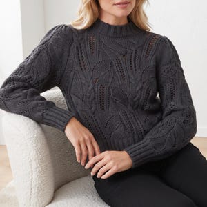 May include: A dark charcoal grey long-sleeve jumper featuring a mock neck, ribbed cuffs, and a prominent knit pattern of textured leaves and openwork detailing across the front and sleeves, constructed with a thick, soft-looking yarn.