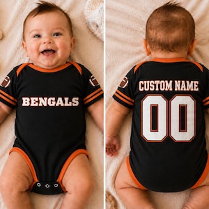 May include: A black baby bodysuit with orange trim, featuring the word BENGALS in white on the front. The sleeves have football graphics and orange stripes. The back displays the text CUSTOM NAME above the large white numbers 00 with orange outlines.