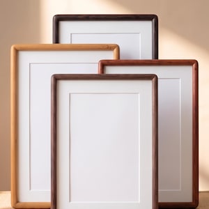 Può includere: Una collezione di quattro cornici rettangolari in legno con angoli arrotondati, ciascuna dotata di un passe-partout bianco. Le cornici variano nelle tonalità del legno, dal legno naturale chiaro al marrone medio e all'espresso scuro.