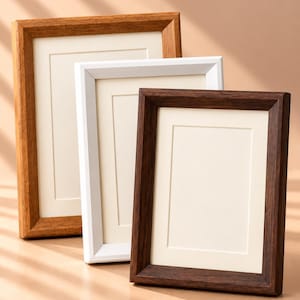 May include: Three rectangular picture frames arranged in a staggered formation. The frames feature a light wood finish, a solid white finish, and a dark wood finish, each containing a cream-coloured mat board with a rectangular inner opening.