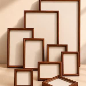 May include: A collection of nine rectangular picture frames made of smooth, medium-toned brown wood. The frames are arranged in a tiered, overlapping display, featuring various sizes including vertical portrait orientations and one square frame.