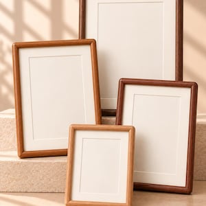 Op de afbeelding: Een verzameling van vier rechthoekige houten fotolijsten in verschillende bruintinten, variërend van licht eiken tot donker walnoot. Elke lijst heeft een strak, eenvoudig ontwerp met een witte passe-partout, gerangschikt in een verspringende opstelling.