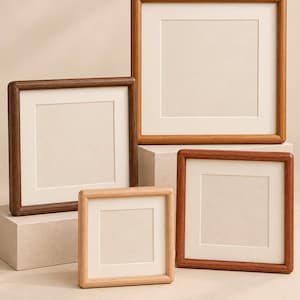 Puede incluir: Una colección de cuatro marcos de fotos cuadrados de madera en varios tamaños y tonos de madera, que van desde el marrón claro al oscuro. Cada marco presenta un borde grueso y redondeado y un paspartú color crema alrededor de un espacio vacío.