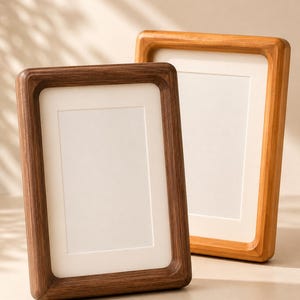 May include: Two rectangular picture frames with rounded inner corners and white matting. One frame is crafted from dark brown wood, while the other is made from a lighter, honey-toned wood. Both frames feature a smooth, solid wood construction.