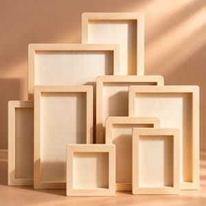 Puede incluir: Una colección de marcos de madera de color claro dispuestos en una pila escalonada. Los marcos son rectangulares y cuadrados, con un acabado de veta de madera natural lisa y un diseño de centro profundo y hueco en varios tamaños.