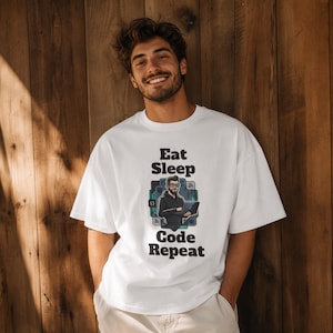 May include: A white short-sleeved t-shirt featuring a graphic print of a person with glasses using a laptop, surrounded by digital icons. The text "Eat Sleep Code Repeat" is printed in black above and below the central graphic illustration.