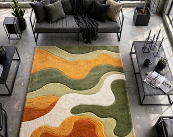 May include: A rectangular area rug featuring a wavy, abstract pattern in shades of mustard yellow, olive green, cream, and burnt orange. The rug has a thick, textured pile and is positioned in the center of a room with industrial decor.