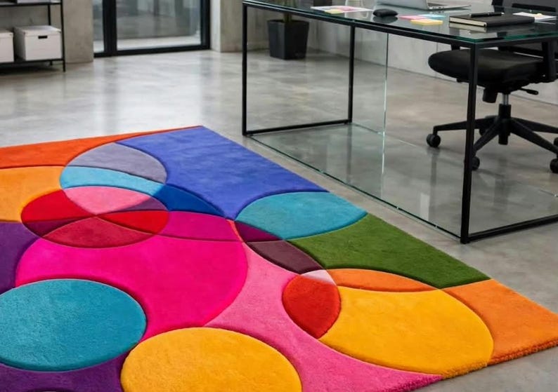 May include: A rectangular area rug featuring a vibrant, multi-colored geometric pattern of overlapping circles and shapes in shades of bright pink, orange, yellow, red, blue, purple, and green, with a soft, plush texture covering the floor surface.