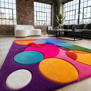May include: A rectangular area rug featuring a vibrant, multi-colored pattern of overlapping circles and ovals in shades of purple, hot pink, bright orange, yellow, turquoise, and white. The rug has a plush, textured pile surface throughout.