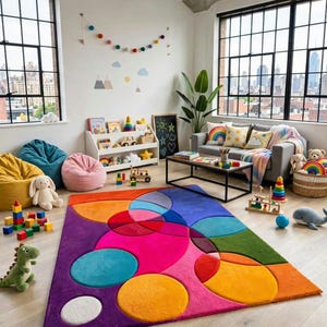 May include: A rectangular area rug featuring a vibrant, multi-colored geometric pattern of overlapping circles and shapes in shades of purple, pink, orange, yellow, blue, and green, set against a light-colored wooden floor in a room.