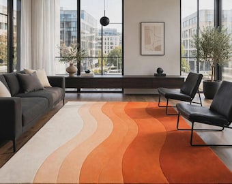May include: A rectangular area rug featuring a gradient of wavy, vertical stripes in shades of cream, light peach, orange, and deep terracotta. The rug is positioned on a dark wood floor in a living room with a dark gray sofa and black chairs.