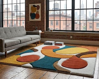 Puede incluir: Una alfombra rectangular de textura de pelo largo con un patrón geométrico de formas abstractas en tonos naranja quemado, amarillo mostaza, verde azulado profundo y marrón oscuro sobre un fondo blanco, sobre un suelo de madera.