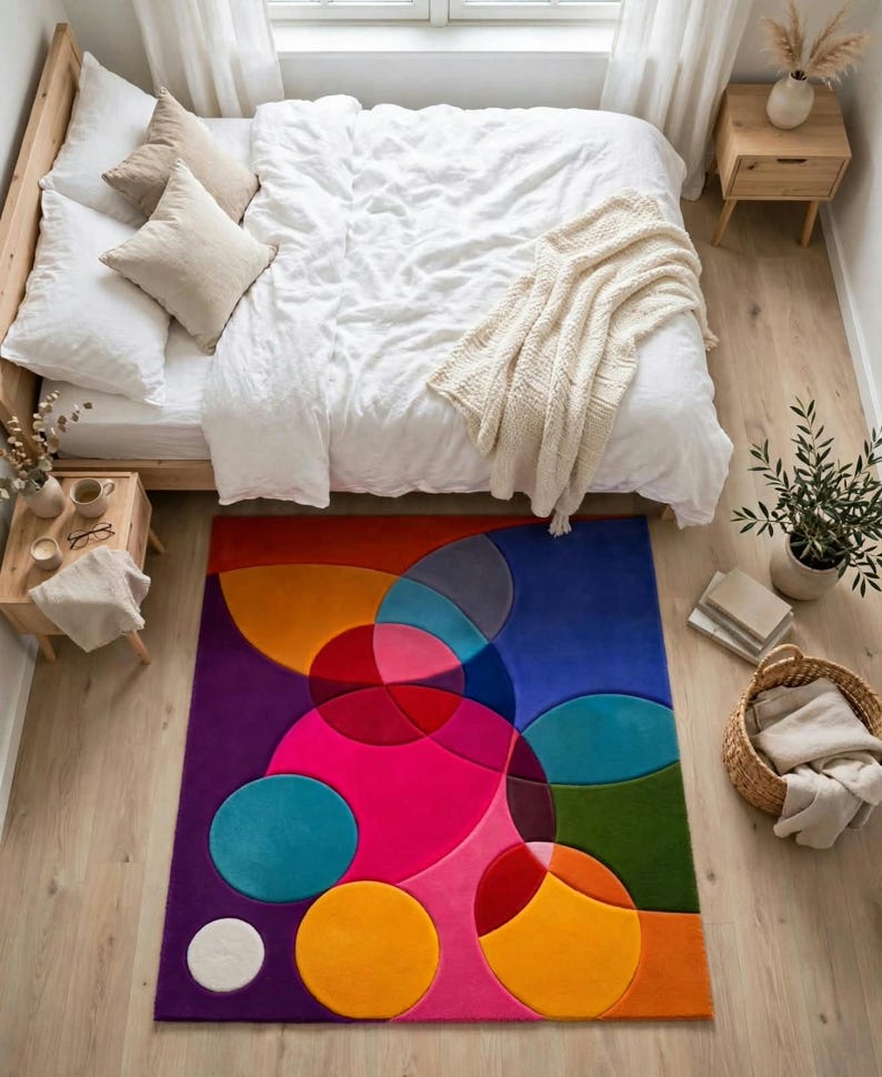 May include: A rectangular area rug featuring a vibrant geometric pattern of overlapping circles and semi-circles in shades of magenta, purple, orange, blue, red, and green, placed on a light-colored wooden floor in a bedroom setting.