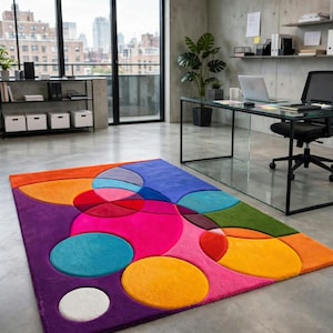 May include: A rectangular area rug featuring a vibrant, multi-colored geometric pattern of overlapping circles and semi-circles in shades of bright pink, orange, purple, blue, green, and white, with a soft, plush texture covering the entire surface.
