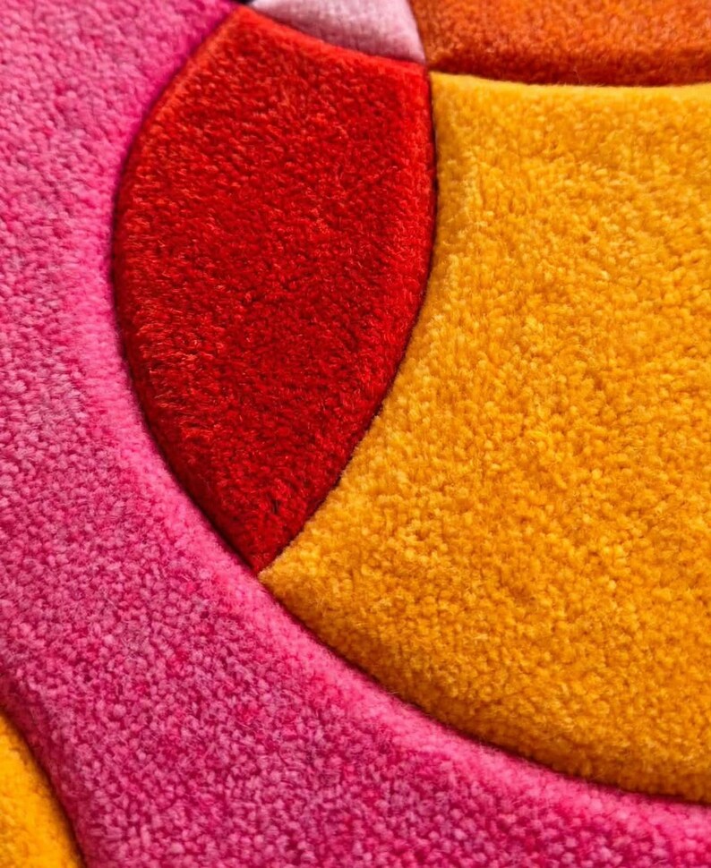 May include: A tufted textile rug featuring a geometric pattern with distinct sections of vibrant colors. The design includes a large curved segment in bright red, a textured area in deep pink, and a prominent section in golden yellow.