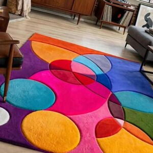 May include: A rectangular area rug featuring a vibrant, multi-colored geometric pattern composed of overlapping circles and semi-circles in shades of hot pink, orange, teal, purple, blue, red, green, and white with a soft, plush texture.
