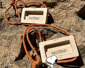 Può includere: Due tavole da arrampicata rettangolari in legno con corde maculate arancioni e verdi. Ogni tavola presenta la scritta SKANDO CLIMBING EQUIPMENT, 15 MM, 7 MM e 21 MM incisa sulla superficie in legno chiaro. È visibile un cane dei cartoni.