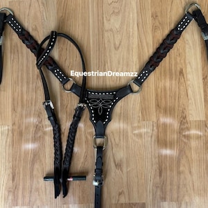 May include: A dark brown leather horse breast collar featuring braided leather accents, white decorative stitching, and silver-toned metal buckles and rings. The center piece displays a stitched floral pattern and the text EquestrianDreamzz.