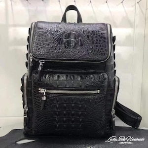 May include: A black backpack featuring a textured crocodile skin pattern. The bag includes a top handle, a main compartment with a zip closure, and a front pocket with a silver zip. The text Lucky Strike Handmade is visible.