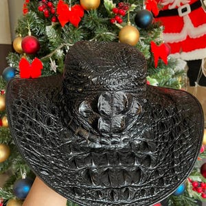 Può includere: Un cappello da cowboy nero con un motivo testurizzato in rilievo che ricorda la pelle di rettile. Il cappello presenta una corona strutturata e una tesa larga e curva. Il testo "Lucky Strike Handmade" è visibile in bianco in basso a destra.