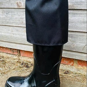 May include: A black rubber rain boot featuring a tall, matte black fabric cuff extension at the top. The cuff is secured with an elasticised, ruffled drawstring closure, providing a protective layer that extends above the glossy black boot shaft.