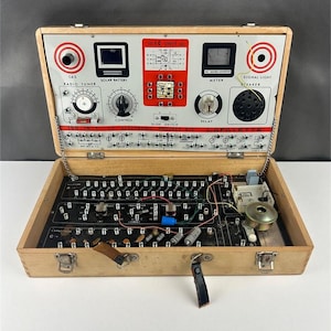 May include: Vintage 150-in-1 IC electronic project kit in a wooden case. The open case reveals a circuit board with various components, dials, and switches. The top panel features a radio tuner, solar battery, and signal light. The case is secured with metal latches and leather straps.