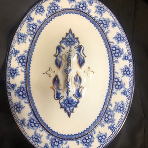 May include: A white oval serving dish with a blue and gold floral pattern. The dish has two handles and a lid with a decorative knob.