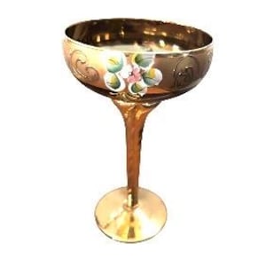 May include: A metallic gold-toned stemmed goblet featuring a wide, shallow bowl with a hand-painted floral motif in shades of green, white, and pink. The stem has a twisted, textured design leading to a circular base, creating a reflective finish.