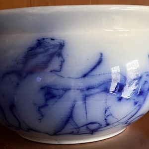 May include: A white ceramic chamber pot with a blue and white floral design. The pot has a handle on the side and a rounded body.