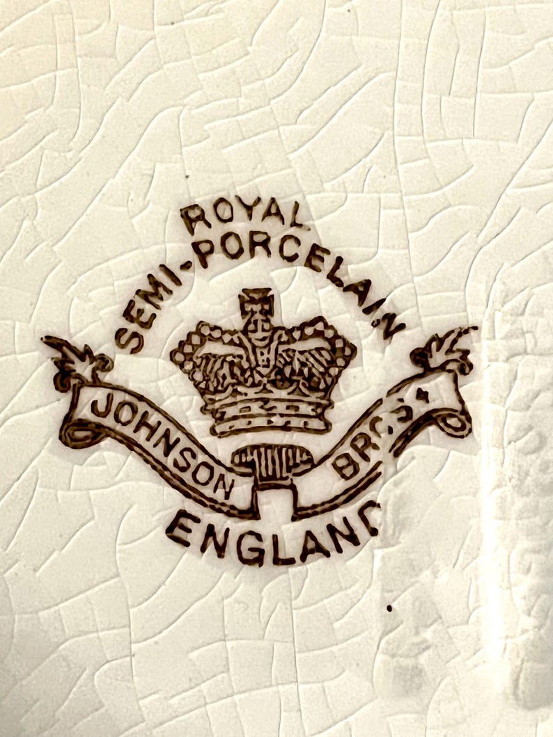 May include: Close-up of a white ceramic surface with a cracked texture. The image features a brown emblem with the words "Royal Semi-Porcelain" and "Johnson Bros England" surrounding a crown.
