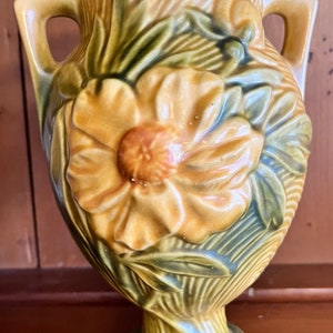 May include: A brown and green ceramic vase with a floral design. The vase has two handles and a wide base.