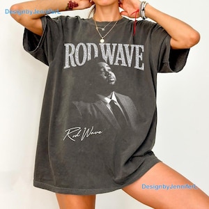 May include: A charcoal gray short-sleeve t-shirt featuring a black and white photographic print of a person in a suit. The text ROD WAVE is printed in a large, distressed white font above the image, with the signature Rod Wave below it.