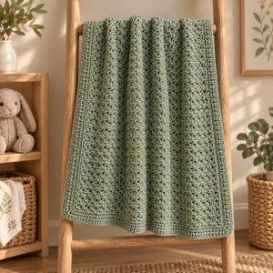 May include: A sage green rectangular crochet blanket featuring a textured stitch pattern throughout the center and a solid, flat-stitched border along all four edges. The blanket is draped over a wooden ladder, displaying its soft, uniform color.