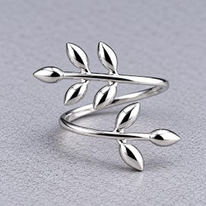 May include: A polished silver-tone ring featuring an open, bypass-style band. The two ends of the ring are shaped like delicate, smooth branches, each adorned with three small, rounded leaf-shaped accents that curve around the finger.