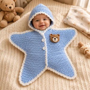 May include: A light blue star-shaped crochet baby bunting with a hood, white scalloped trim, two white buttons, and a small brown bear face appliqué on the chest. The garment features a textured stitch pattern and is designed to wrap around an infant.