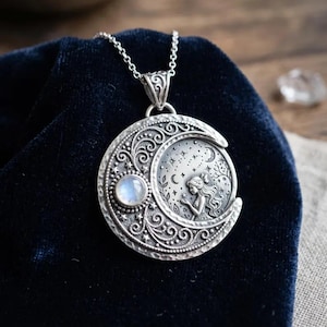 May include: A circular silver pendant necklace featuring a crescent moon design with intricate scrollwork, a small round iridescent moonstone, and a relief carving of a figure reaching towards stars and a smaller moon set against a dark background.