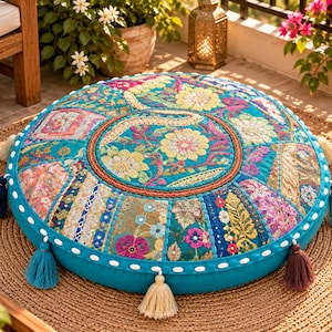 May include: A round floor cushion featuring a vibrant turquoise base with intricate patchwork embroidery in shades of pink, yellow, and gold. The cushion is accented with multiple colorful fabric tassels around the edge and white stitching.