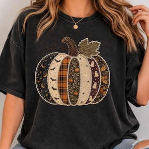 Peut inclure: Un t-shirt à manches courtes gris anthracite orné d'un grand motif central représentant une citrouille composée de panneaux verticaux. Les panneaux présentent divers motifs dont des lunes, étoiles, chauves-souris, carreaux, fleurs, toiles d'araignée et fantômes.
