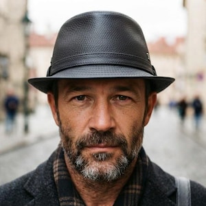 Könnte beinhalten: Ein dunkel anthrazitfarbener Fedora-Hut mit strukturierter Oberfläche und einem passenden dunklen Band um die Krone. Der Hut verfügt über eine strukturierte Krempe und ein kleines Metalldetail an der Seite für einen klassischen Look.