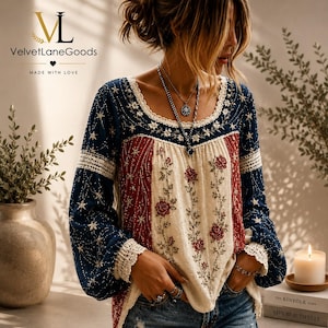 Pode incluir: Uma blusa de manga comprida em tecido azul-escuro com estrelas brancas bordadas e um painel central em tom creme adornado com bordados florais vermelhos. A peça inclui um intrincado acabamento em renda branca no decote e nos punhos.
