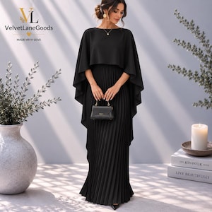 Könnte beinhalten: Ein bodenlanges schwarzes Kleid mit plissiertem Rock und einem angesetzten, capeartigen Überwurf. Das Kleid hat einen Rundhalsausschnitt und wird mit einer kleinen, strukturierten schwarzen Handtasche mit goldfarbenem Verschluss kombiniert. Das Logo VelvetLaneGoods ist sichtbar.