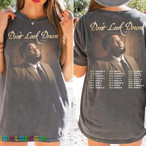 May include: A charcoal gray short-sleeve t-shirt featuring a graphic of a man in a suit with the text "Don't Look Down" and "ROD WAVE". The back of the shirt displays the same graphic with a list of tour dates and cities printed below it.