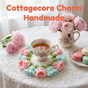 Könnte beinhalten: Ein runder, gehäkelter Untersetzer mit weißer Mitte und einem Rand aus abwechselnd hellrosa und hellblauen Garnblumen. Eine Teetasse mit Blumenmuster steht auf dem Untersetzer, daneben ein Krug mit rosa Pfingstrosen und Macarons.