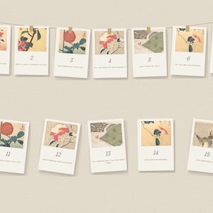 Puede incluir: Un conjunto de doce tarjetas rectangulares colgadas de una cuerda, cada una con una ilustraci&oacute;n japonesa de flores o p&aacute;jaros, un n&uacute;mero y una instrucci&oacute;n impresa. Las tarjetas son blancas con bordes beige y cinta adhesiva.